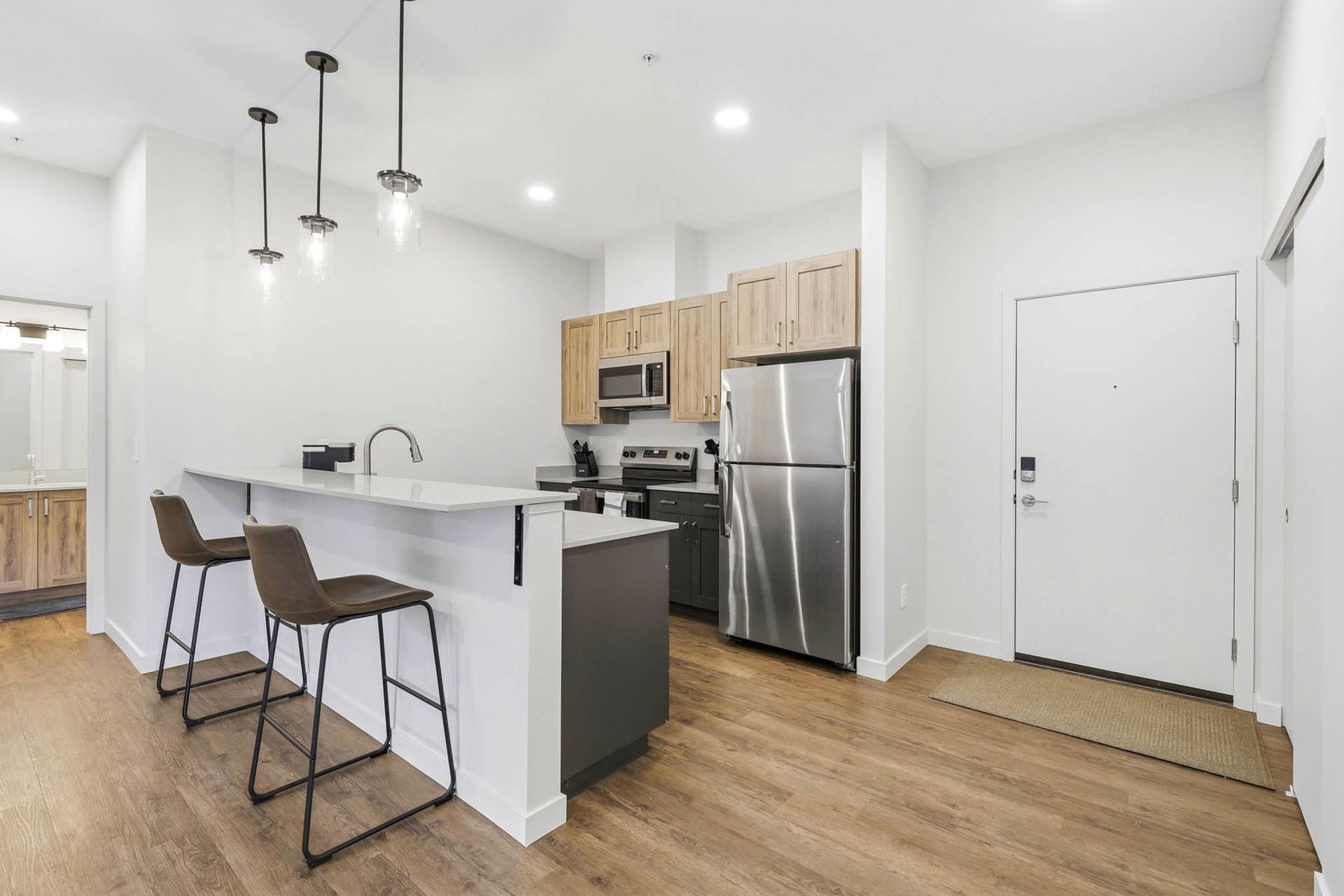 Bright modern kitchen with island, bar stools, stainless steel appliances, and wood floors
