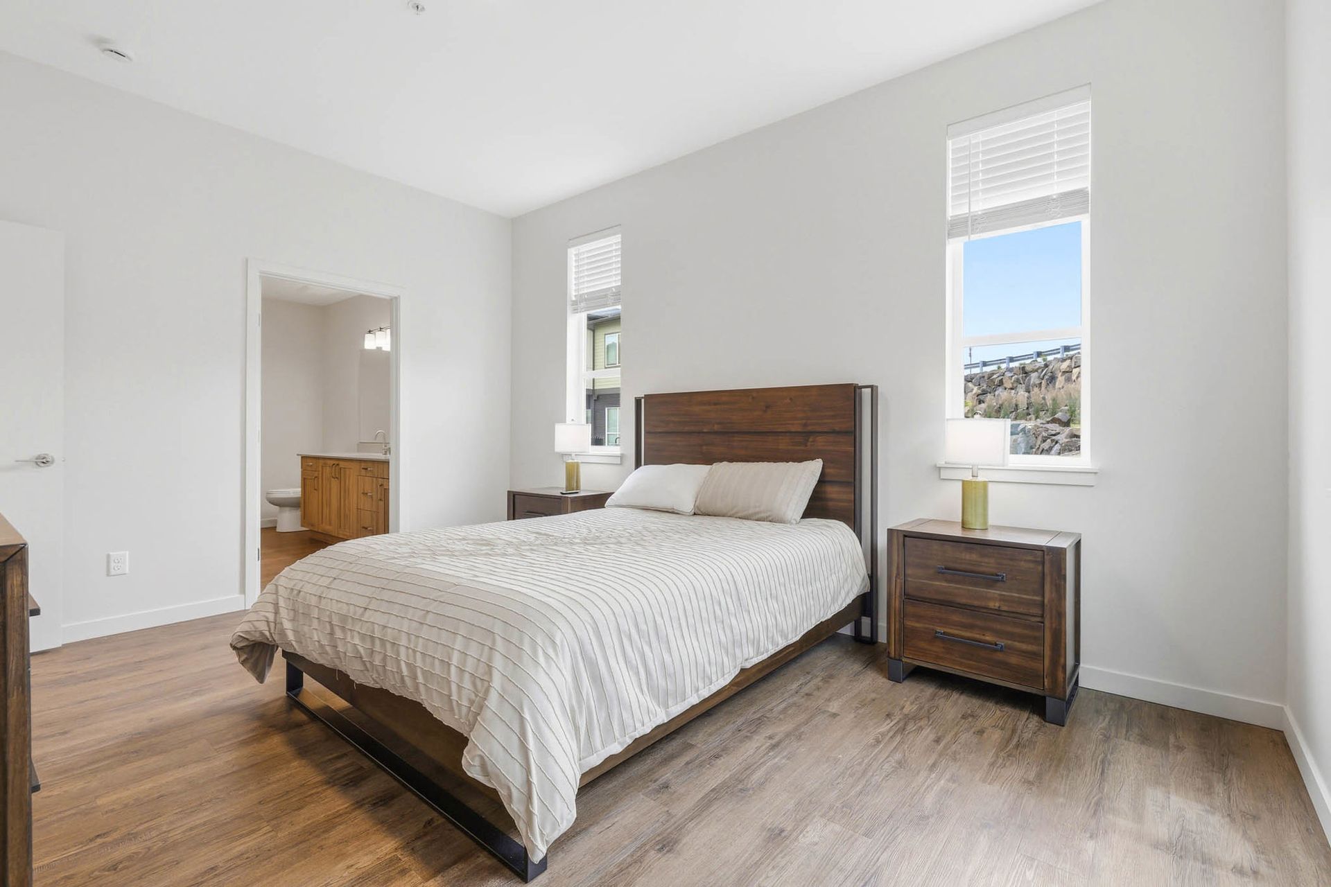 Bright bedroom with a made bed, wood flooring, and two windows