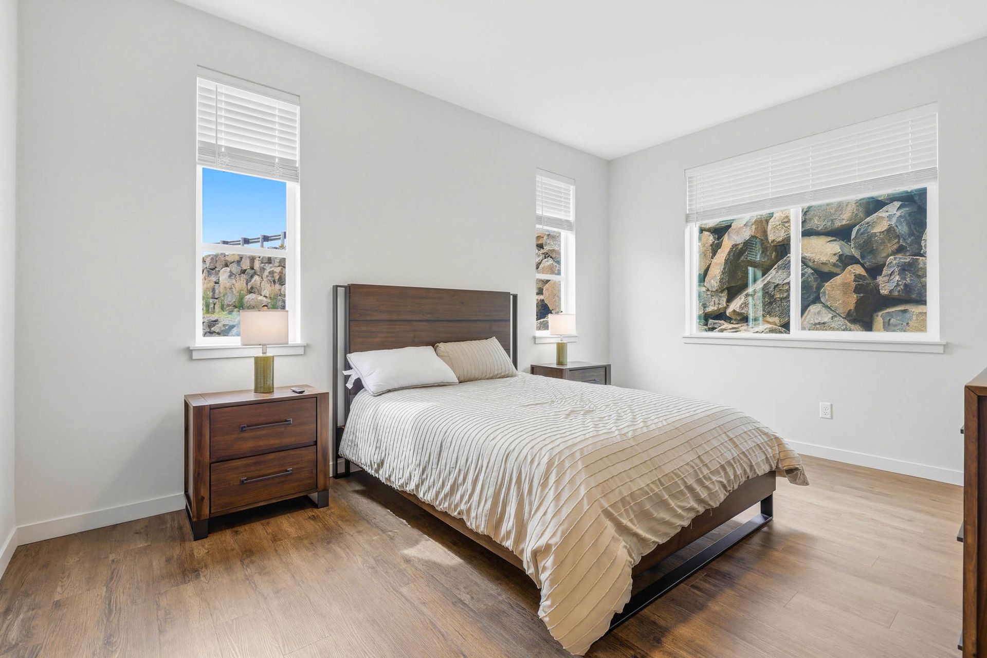 Bright bedroom with a wooden bed, nightstand, and large windows letting in daylight.