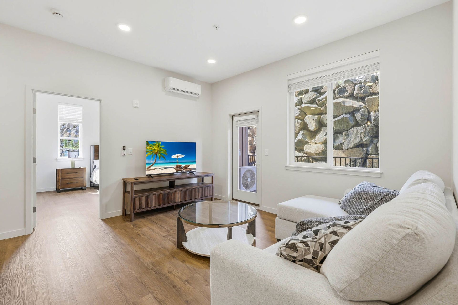 Bright living room with white sofa, TV console, wall art, and open doorway to another room