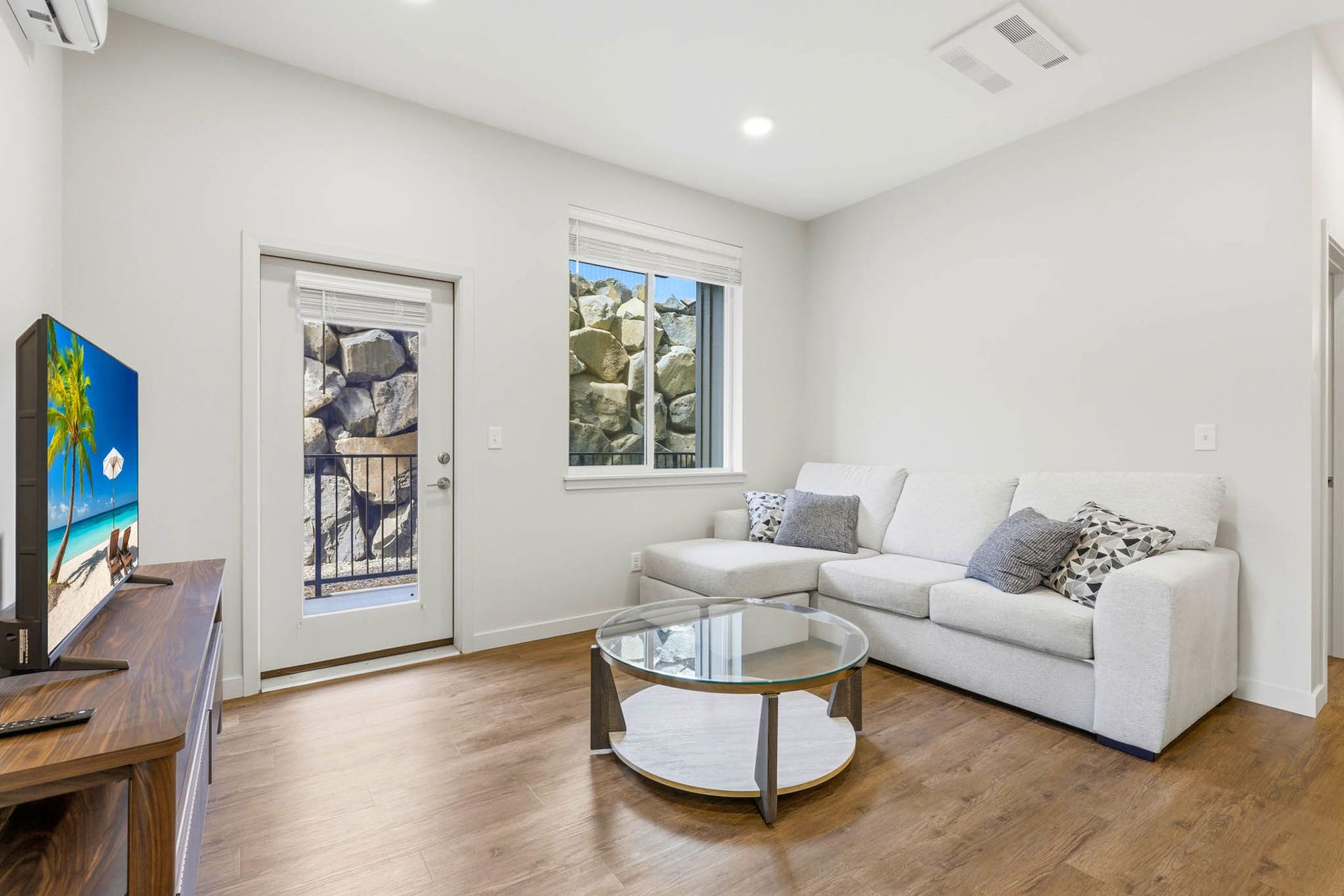 Bright modern living room with white sofa, round coffee table, wood floor, and wall-mounted TV