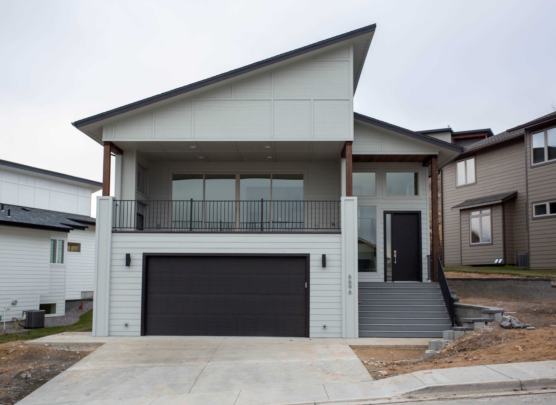 A modern two-story home with a white exterior, slanted roof, upper balcony, and a ground-level garage in a suburban area.