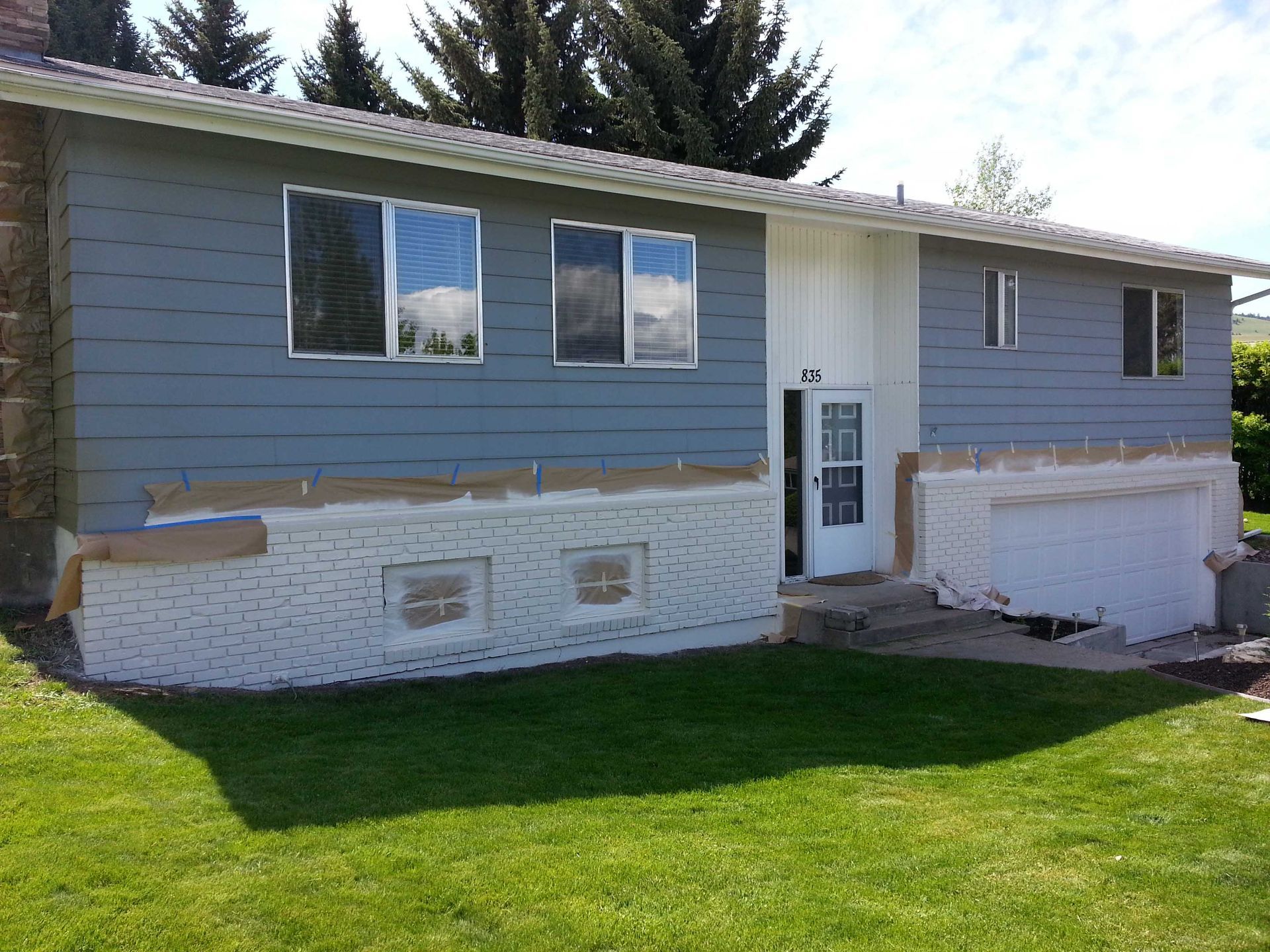 A split-level house with blue siding and freshly painted white brick at the base, currently undergoing exterior renovation.