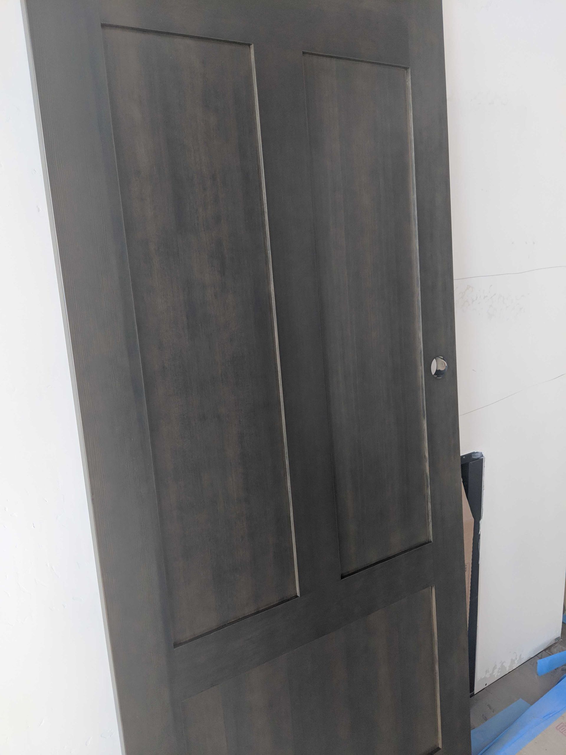 A dark brown, vertical wood-grained door with two tall upper panels and one rectangular bottom panel stands indoors.