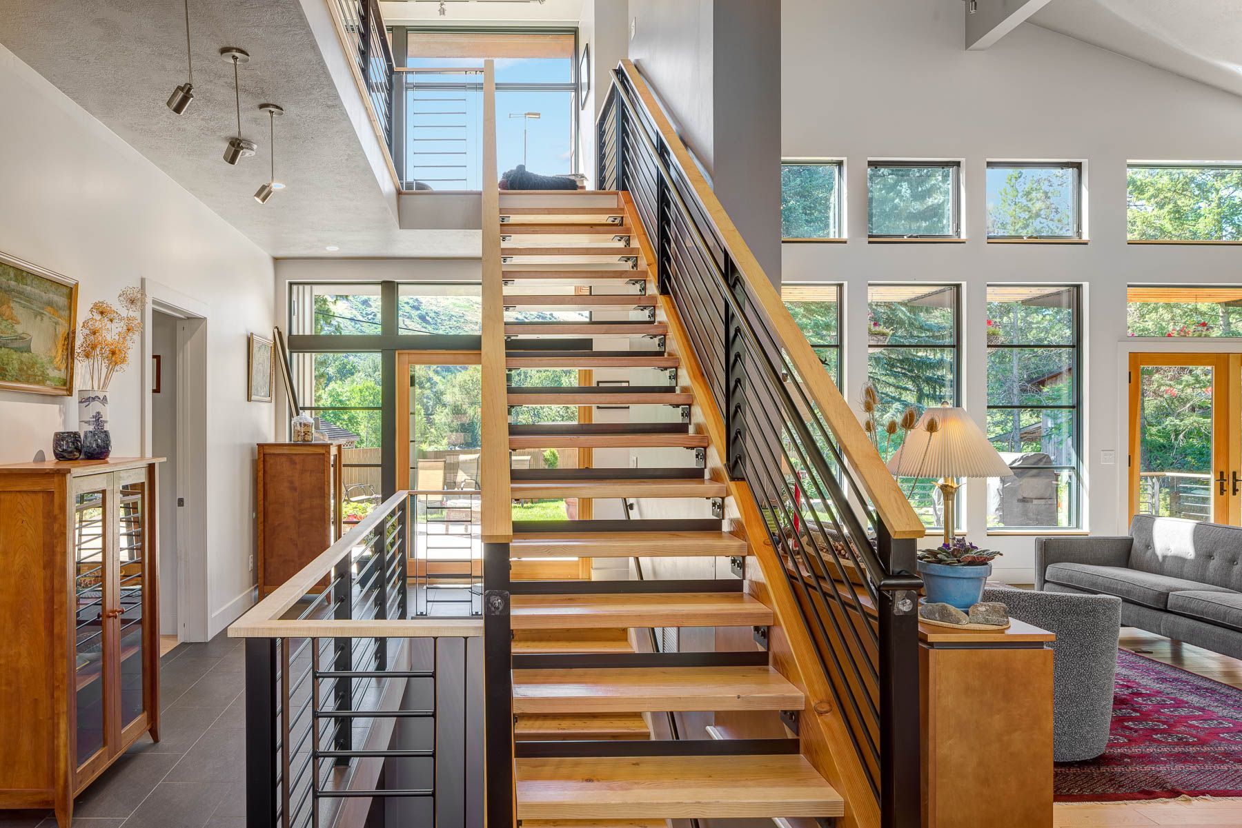 A modern foyer features a central wooden staircase with metal railings leading upward between a living area and entry.