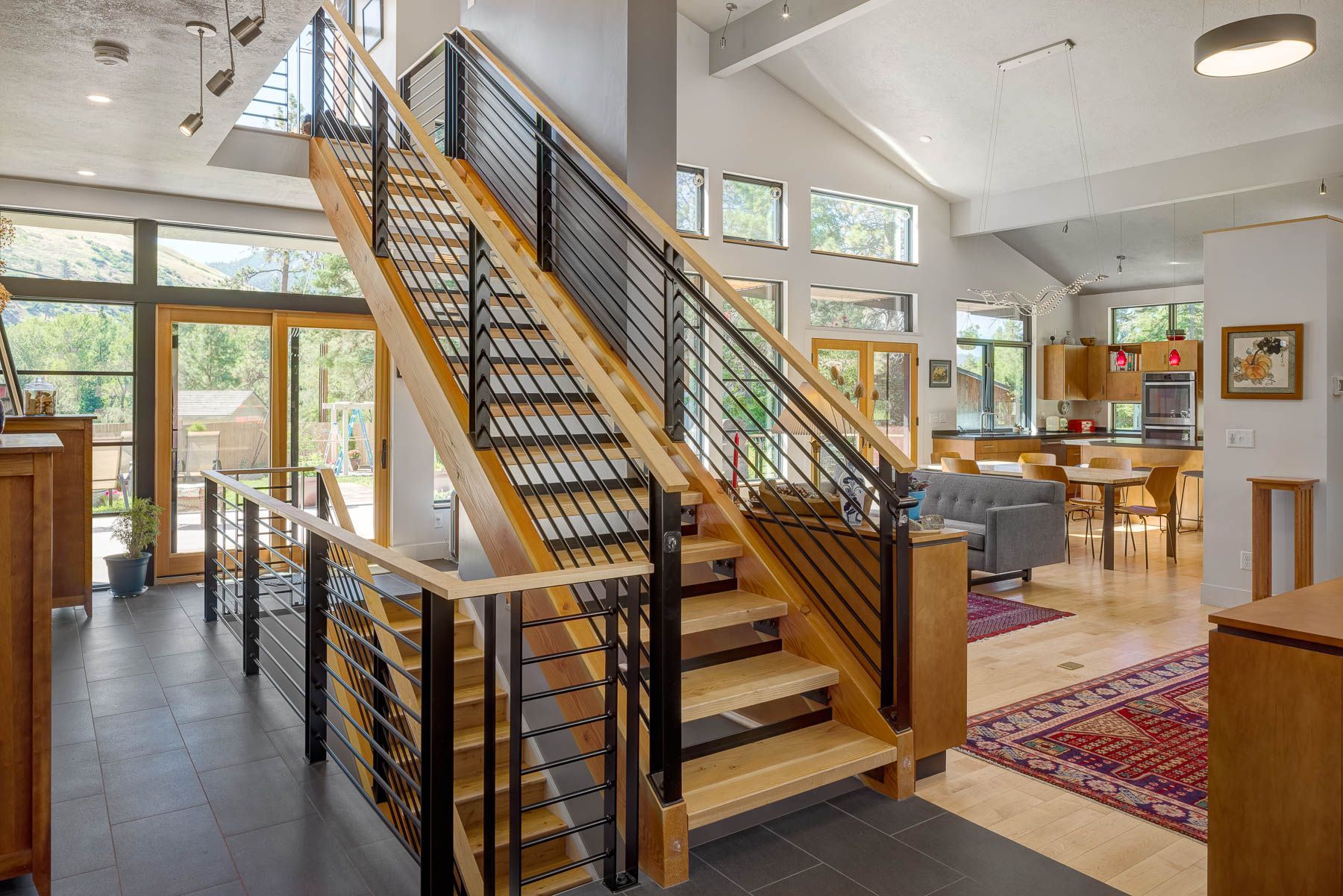 Modern house interior featuring a wooden staircase with black cable railings, hardwood floors, and an open-plan kitchen.
