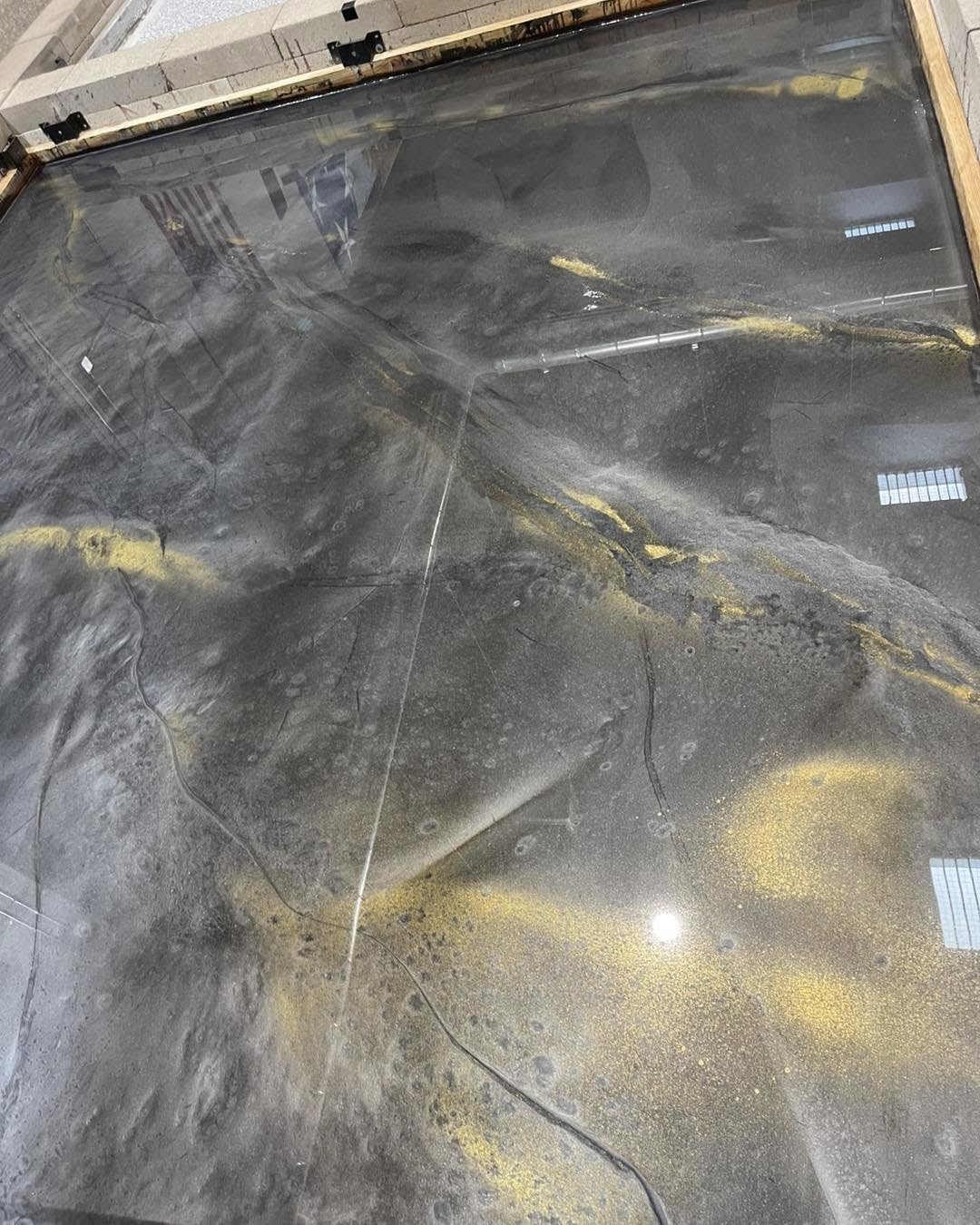 Dusty black work surface with yellow stains and crumpled clear plastic sheeting under bright light