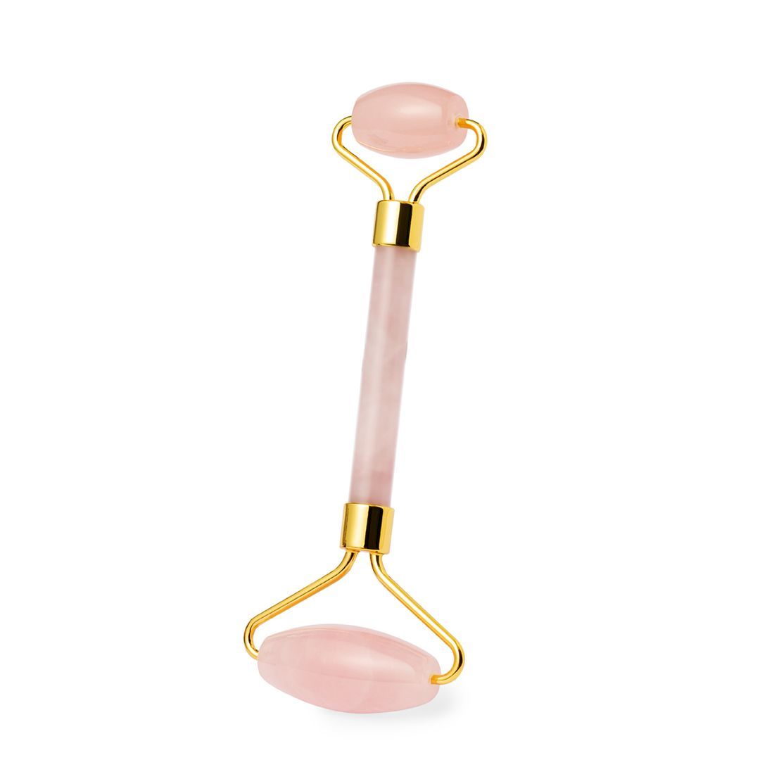 Un rodillo facial de cuarzo rosa de doble extremo con piedras de color rosa claro y detalles metálicos en tono dorado sobre un fondo blanco.