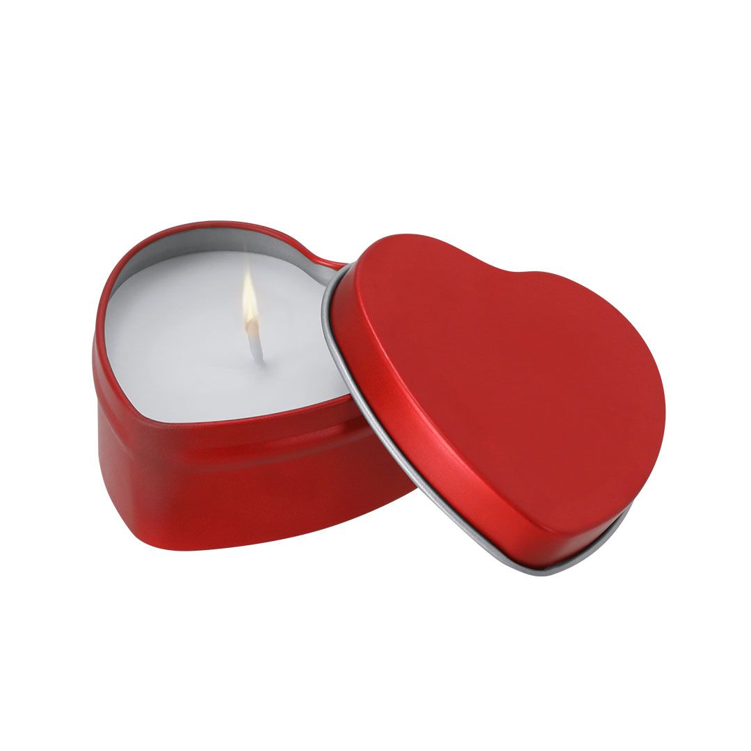 Una vela encendida en una lata roja con forma de corazón, con su tapa apoyada a su lado.