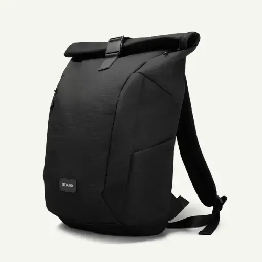 Una mochila negra enrollable de diseño minimalista, vista de perfil sobre un fondo liso de color claro.