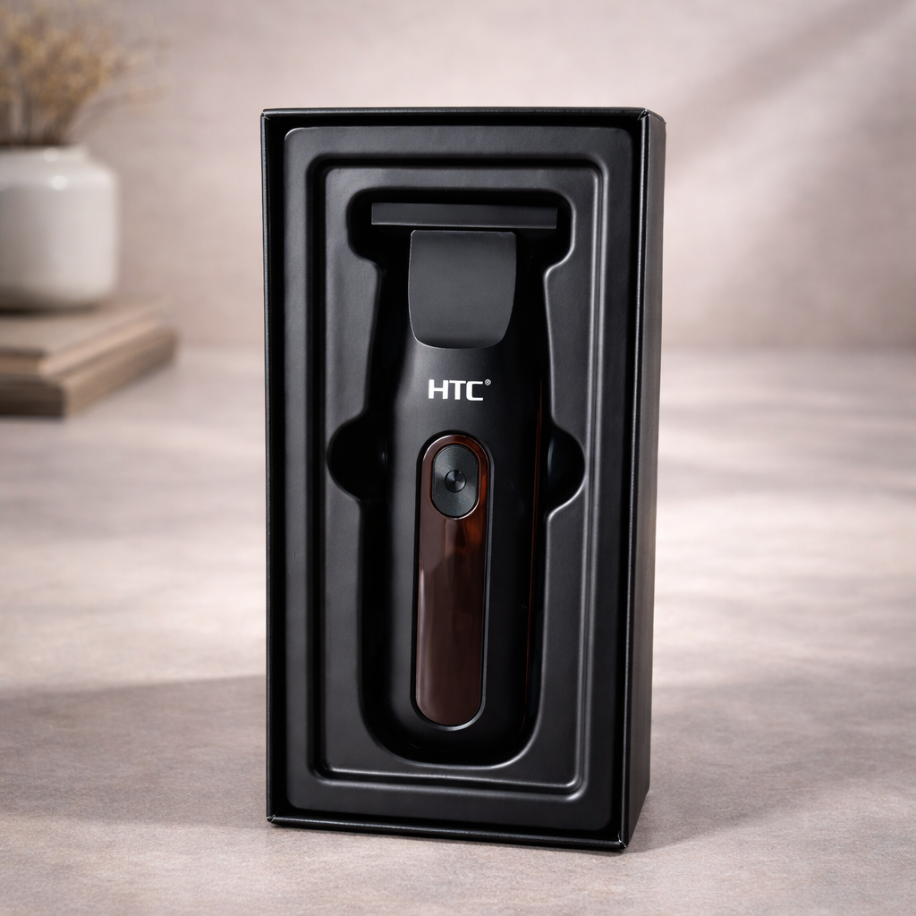 Una recortadora de barba eléctrica HTC negra reposa dentro de su embalaje de plástico moldeado negro sobre una superficie neutra.