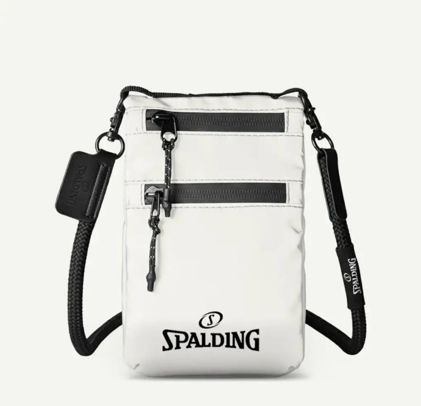 Un bolso bandolera blanco de Spalding para el teléfono móvil con dos bolsillos negros con cremallera y una correa de cuerda negra sobre un fondo gris claro.