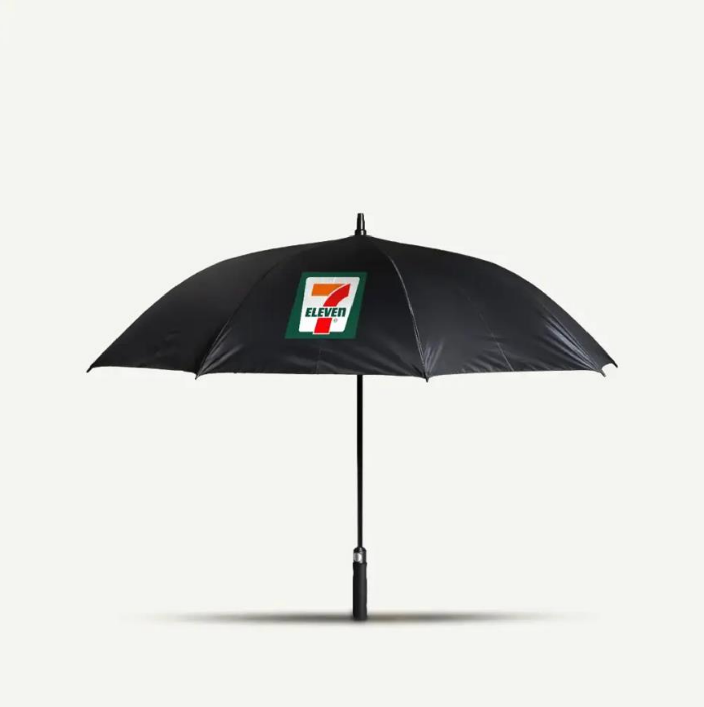 Un paraguas negro de tamaño normal con el logotipo de 7-Eleven prominentemente exhibido en un lado sobre un fondo liso.