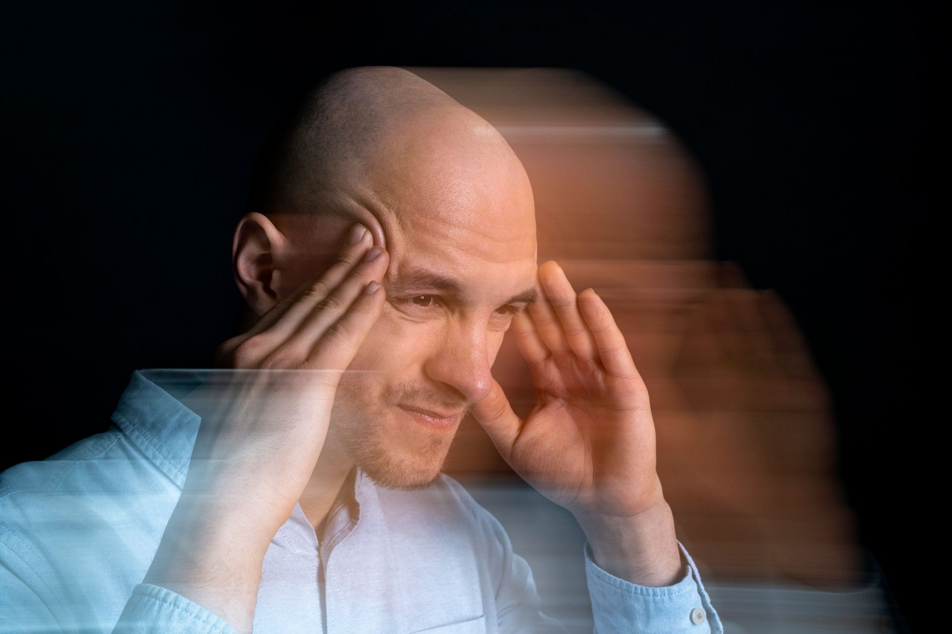 A bald man is holding his head in pain.