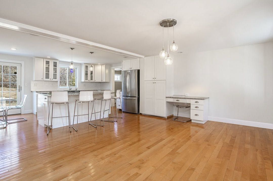 Bright open living room with hardwood floors, white walls, and a kitchen with a breakfast bar.