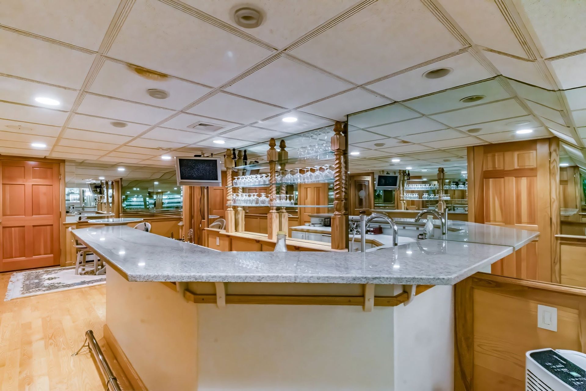 Empty bar with wood paneling, mirrored back wall, and a large gray countertop under recessed ceiling lights