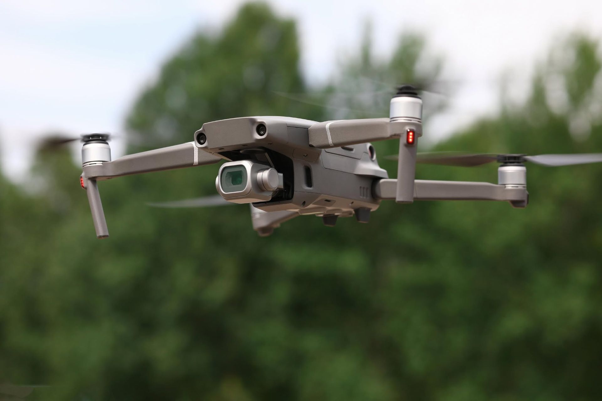 Gray drone flying outdoors with blurred green trees in the background