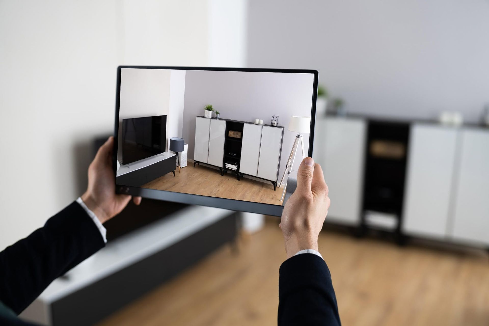 Hands holding a tablet showing a living room interior with a white cabinet and TV.