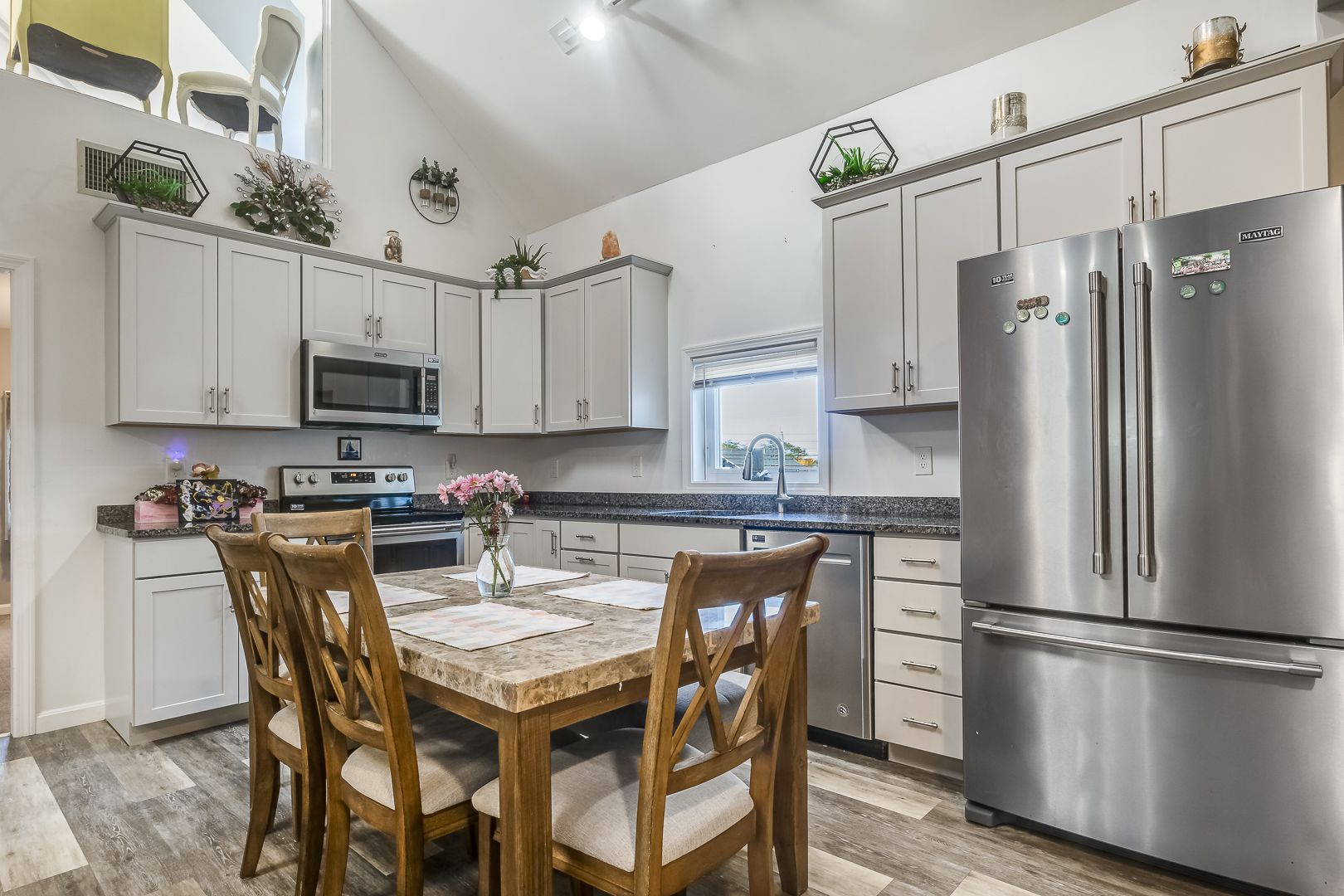 Modern kitchen with gray cabinets, stainless steel refrigerator, and a wooden dining table in the center