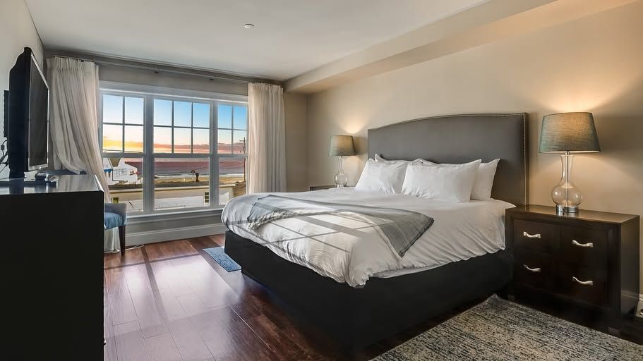 Modern bedroom with a large bed, bedside lamps, and a window overlooking a city at sunset.