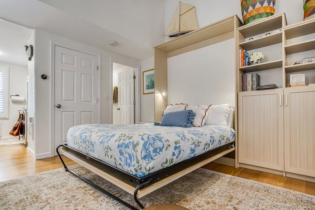 Bright bedroom with a low bed, built-in shelves, beige rug, and white doors.