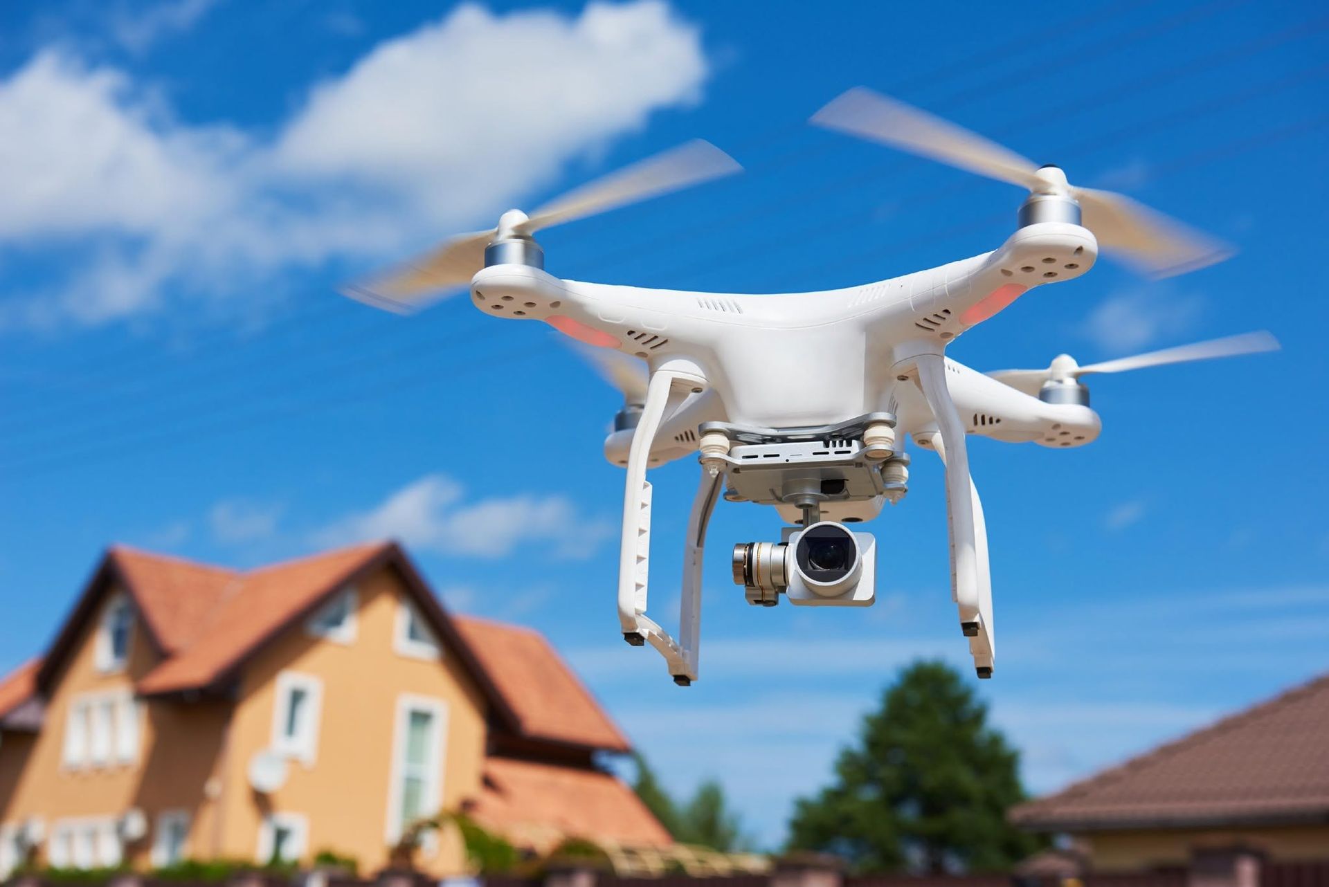 White drone with camera flying above houses on a sunny day