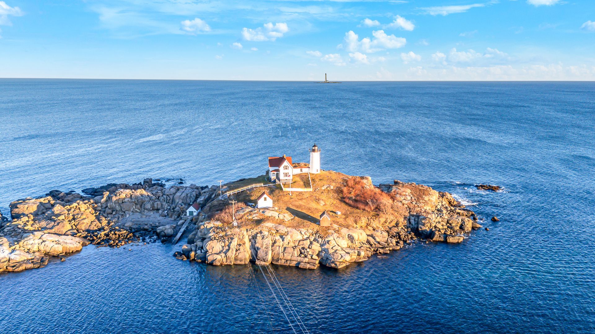 Small white lighthouse on rocky island in blue ocean under a clear sky
