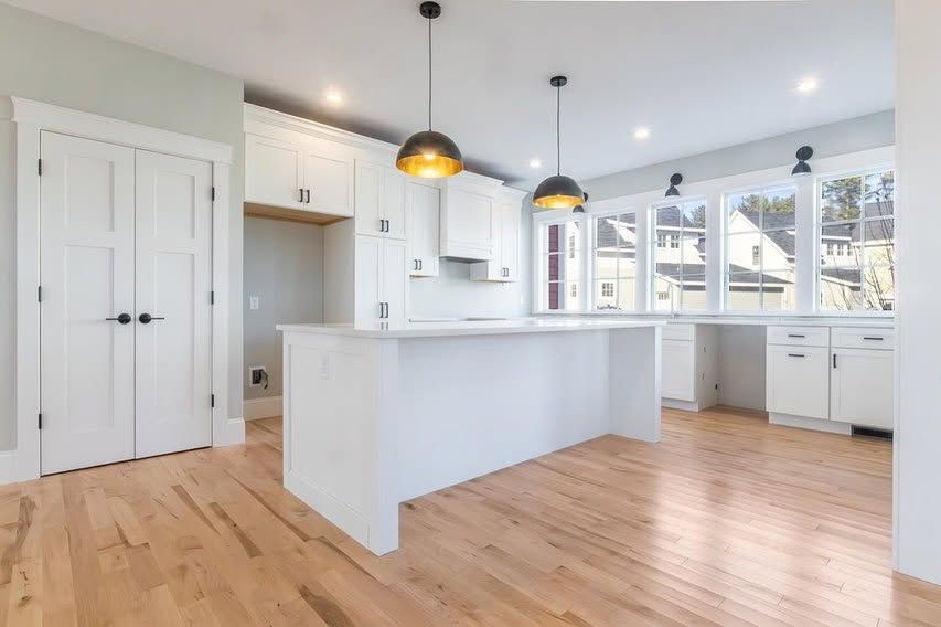 Bright modern kitchen with white cabinets, island, pendant lights, and light wood floors