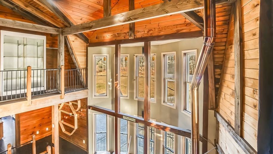 Wooden loft interior with exposed beams, tall windows, and a view of the lower level.