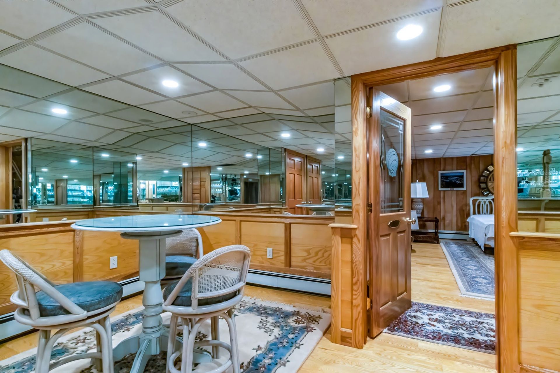 Wood-paneled room with mirrored walls, patterned carpet, and a wooden doorway into a dining area.