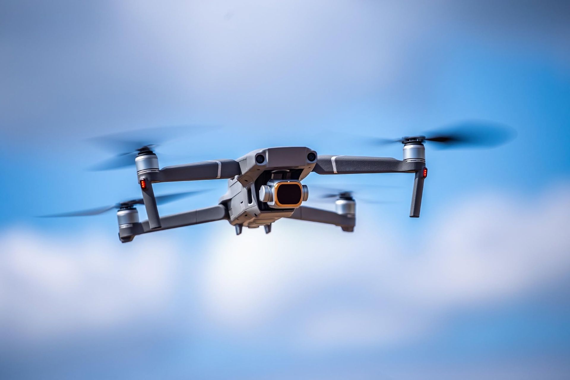 Silver drone flying against a blue sky with blurred propellers