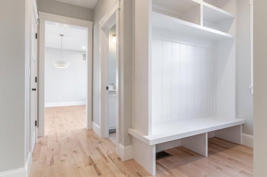 Bright hallway with white built-in bench storage and open doors leading to a light wood-floored room