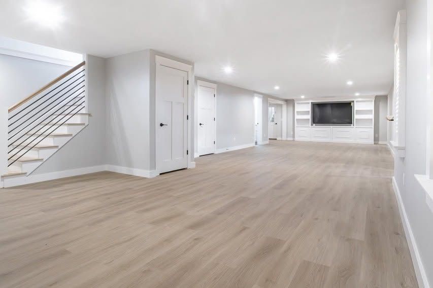 Spacious empty living room with light wood floors, white walls, staircase, and recessed ceiling lights