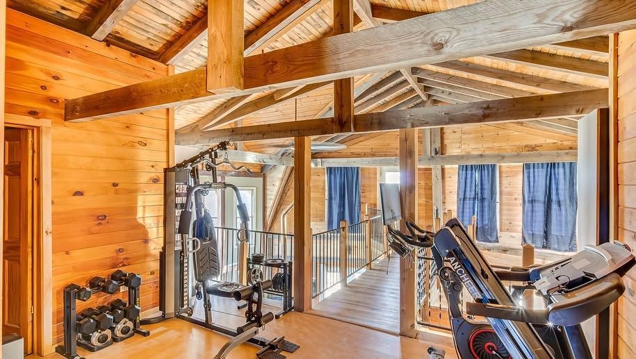 Rustic home gym with wood beams, exercise equipment, and large windows with blue curtains