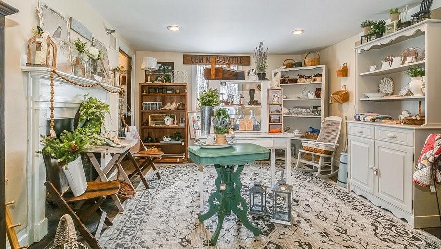 Bright, cozy craft shop with shelves, plants, and a green display table on a patterned rug.