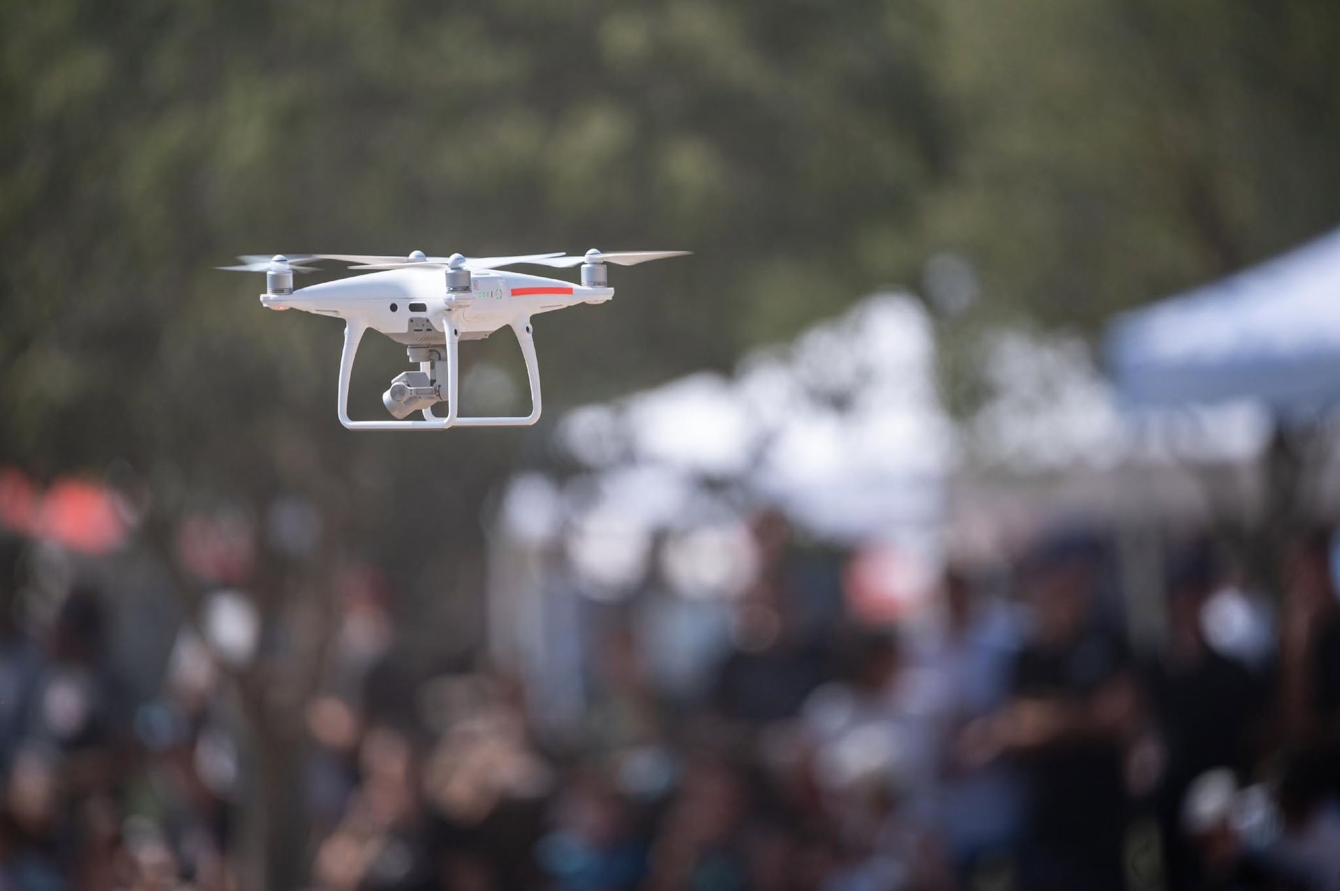 White drone hovering over a blurred outdoor crowd at an event