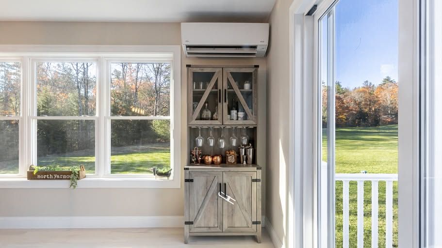 Bright room with windows, a bar cabinet, and a wall-mounted air conditioner overlooking a lawn