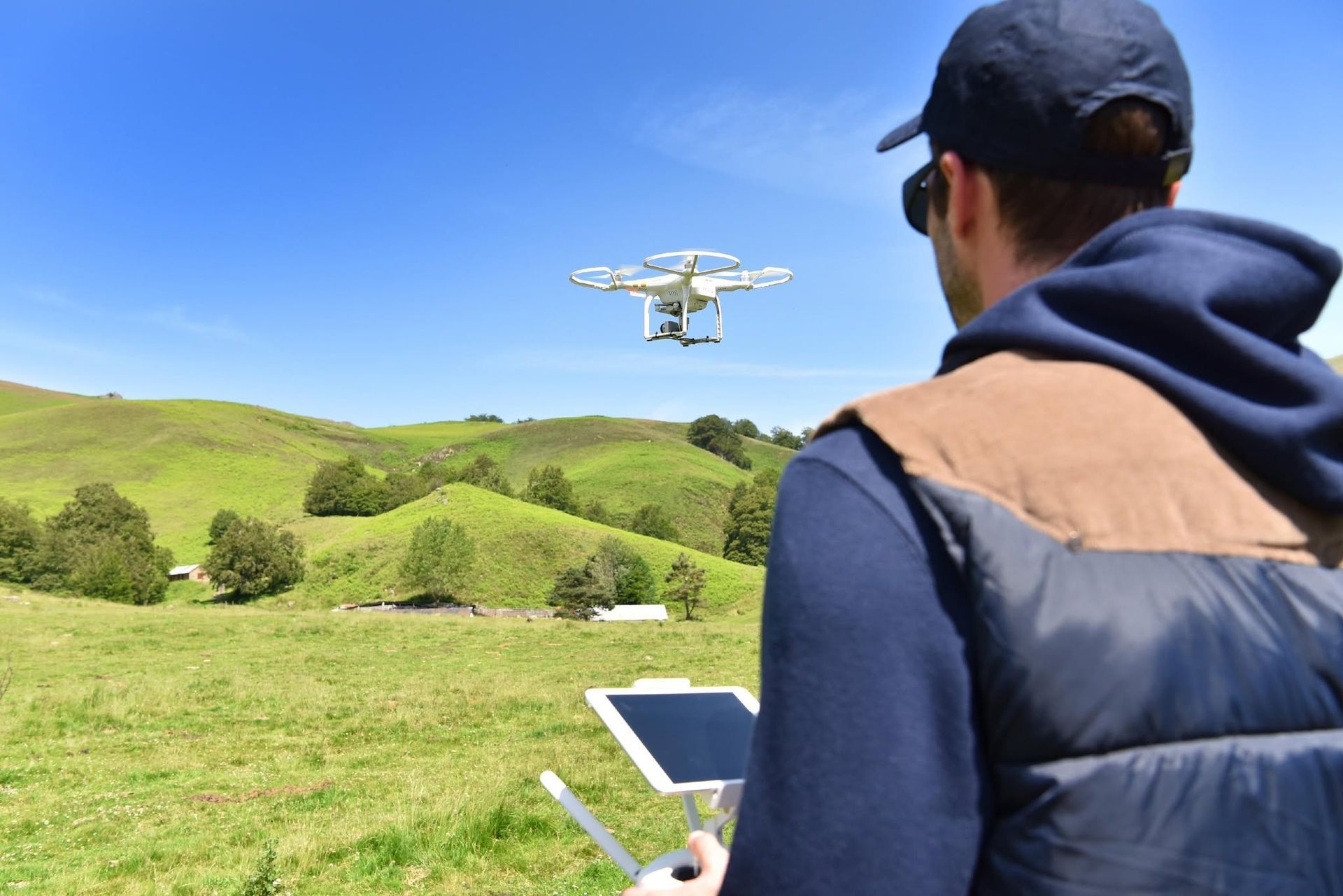 Person flying a drone over green hills, holding a controller in a sunny field