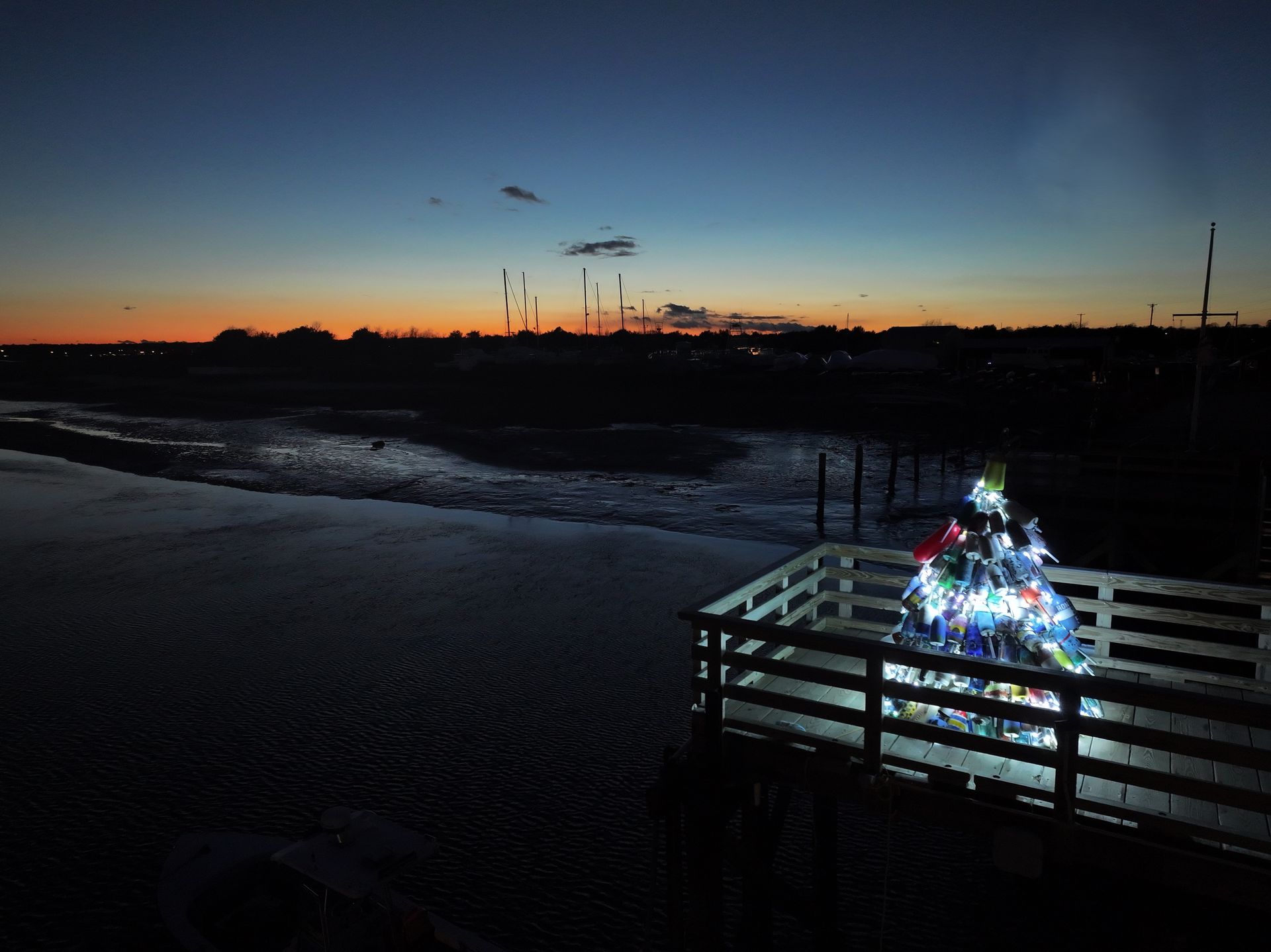 Sunset over a dark beach, with a lit holiday display on a wooden deck in the foreground