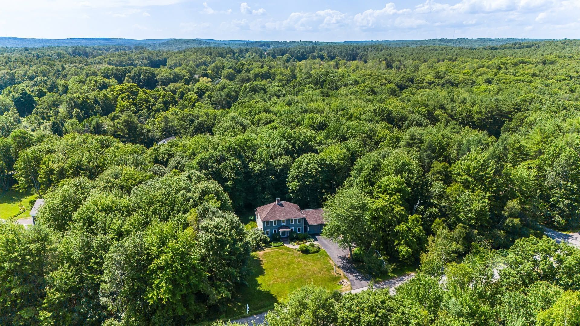 Aerial view of a house surrounded by dense green forest under a blue sky