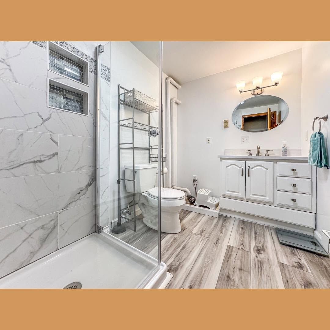 Bright modern bathroom with glass shower, white vanity, toilet, and wood-look floor tiles