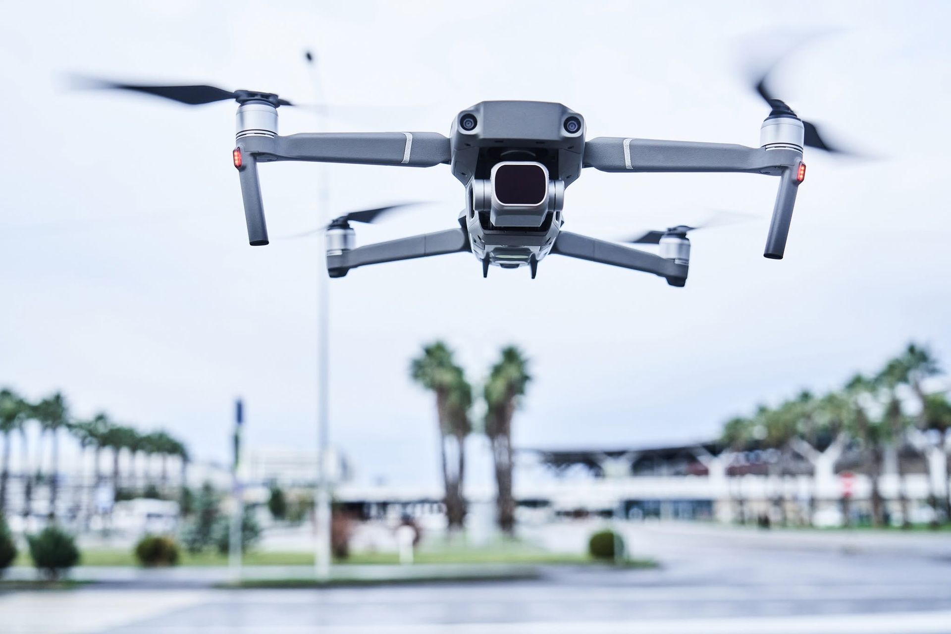 Drone flying low over a blurred outdoor plaza with palm trees and buildings in the background