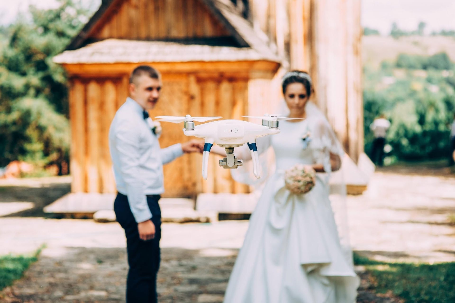 Wedding couple holding a small airplane model outdoors in front of a wooden chapel