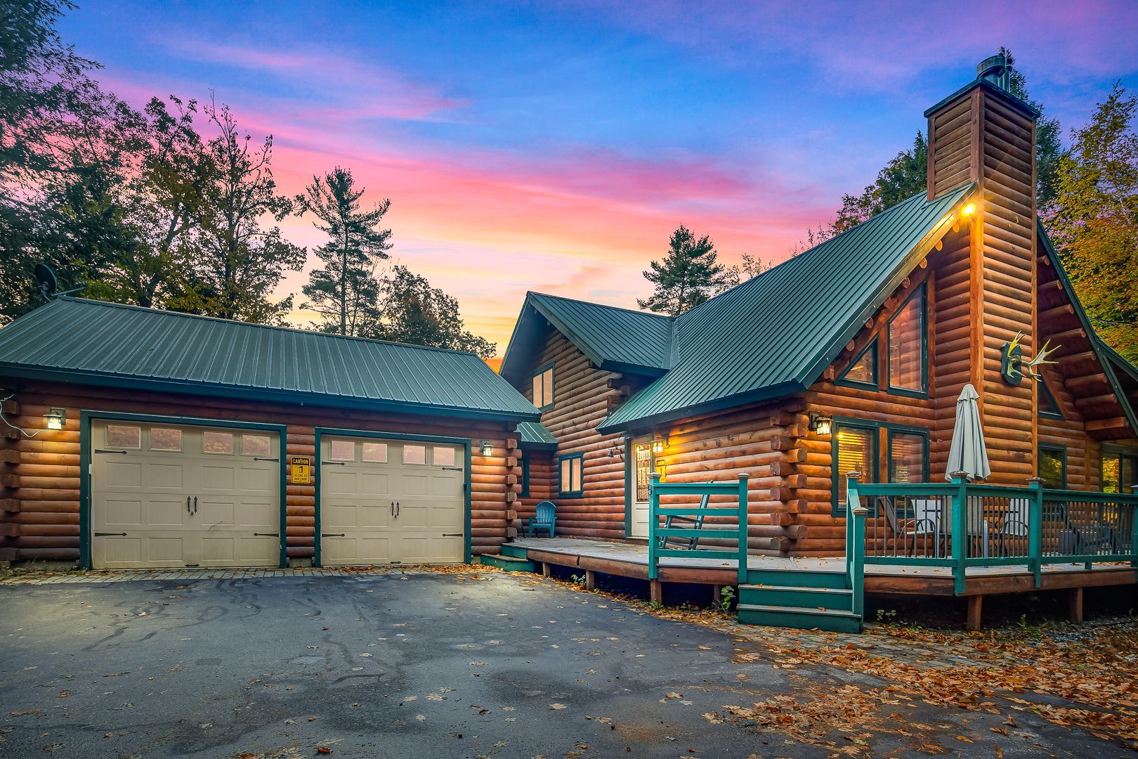 Log cabin home with garage at dusk under a pink-blue sky, surrounded by trees and autumn leaves