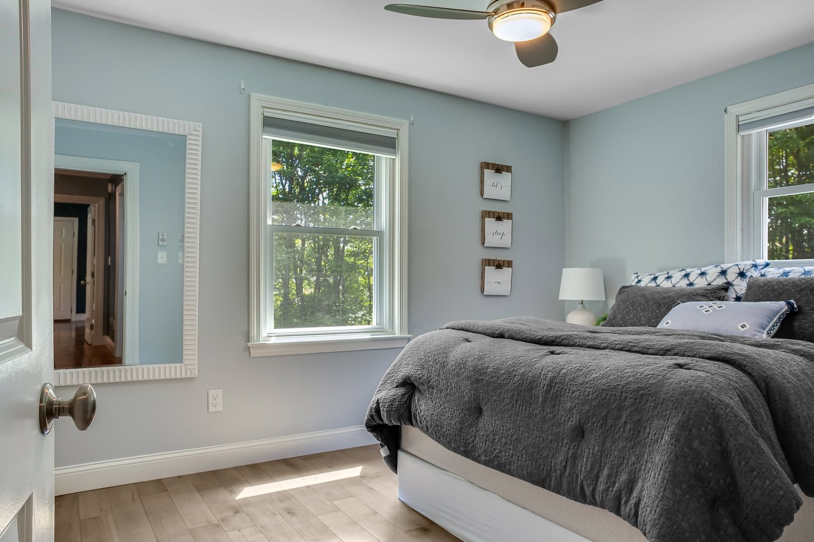 Bright bedroom with light blue walls, two windows, white trim, and a bed with gray bedding
