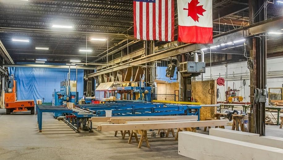 Industrial workshop with blue steel frames, machinery, and U.S. and Canadian flags hanging overhead.