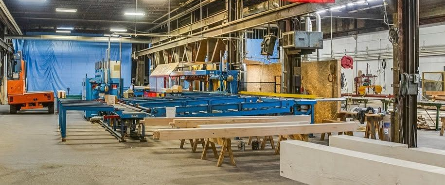 Industrial workshop with blue steel beams, machinery, and stacked materials in a large factory space