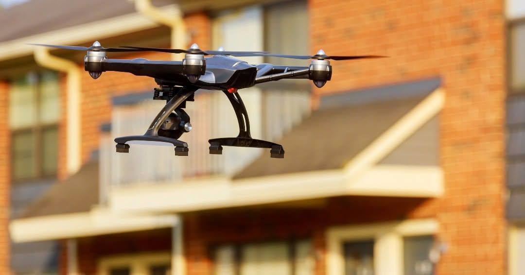 Black quadcopter drone flying in front of a brick building