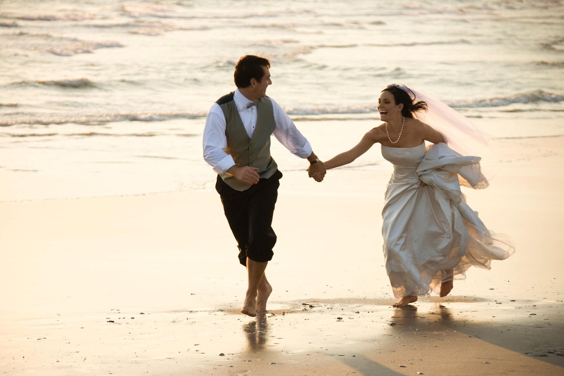 Couple holding hands and running barefoot along a beach at sunset