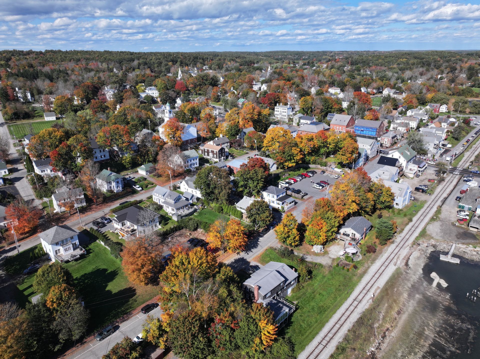 Aerial view of a suburban neighborhood with autumn trees, houses, and a railroad line under a cloudy sky
